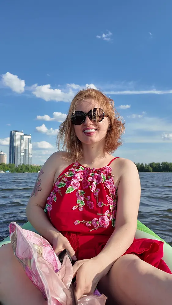 Улыбающаяся Нелли Верховская в красном платье на речном каяке.